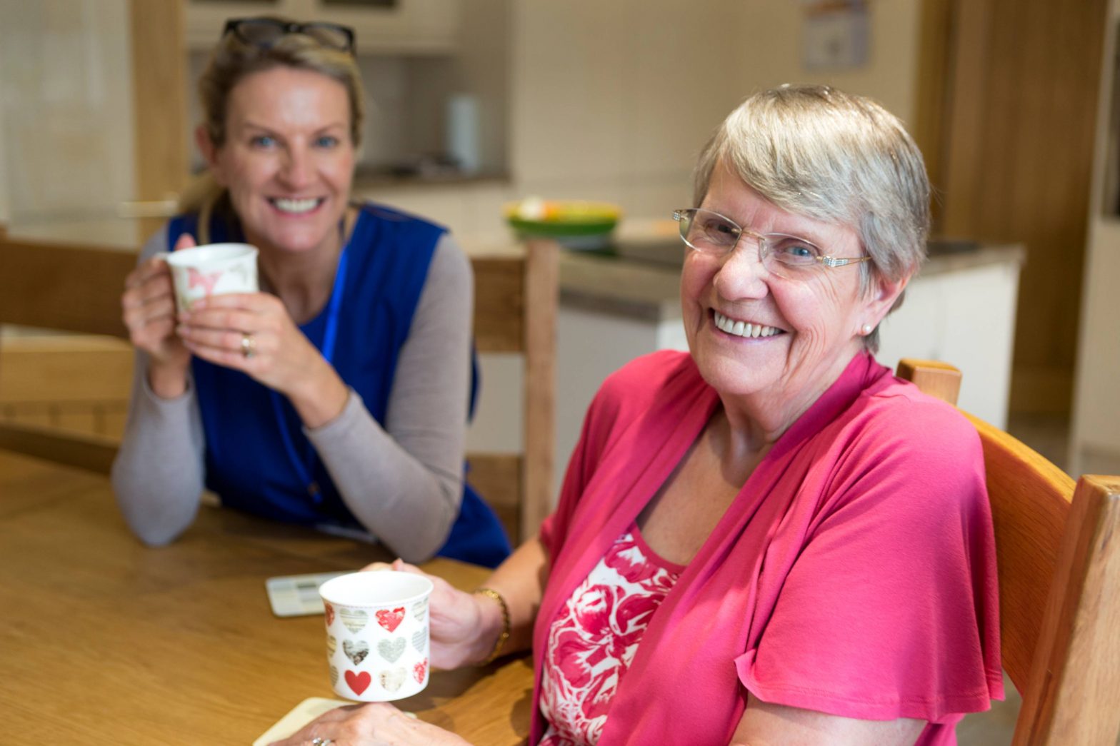 Aged person and support worker sharing coffee in house