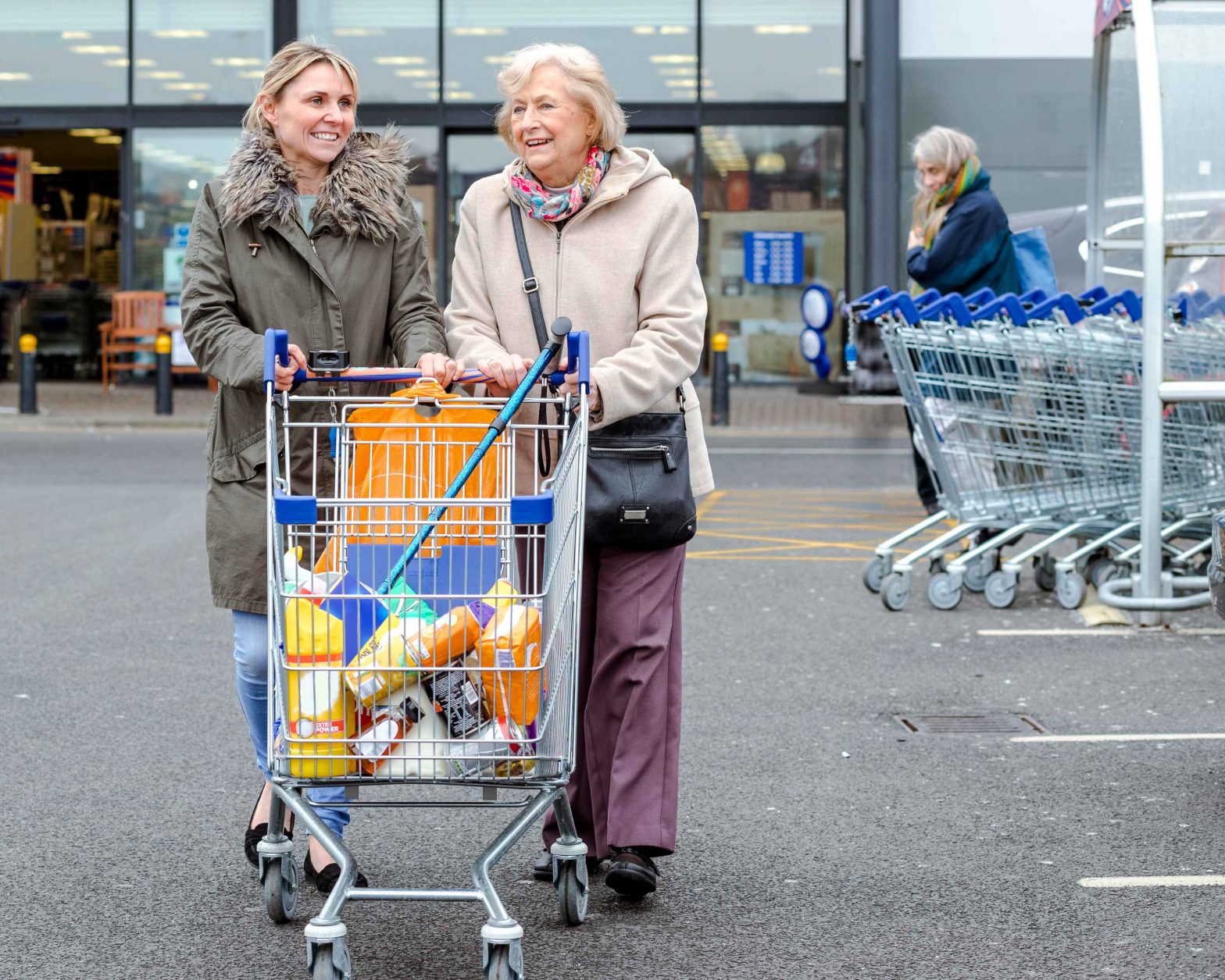 Aged person and support worker pushing shopping cart in carpark