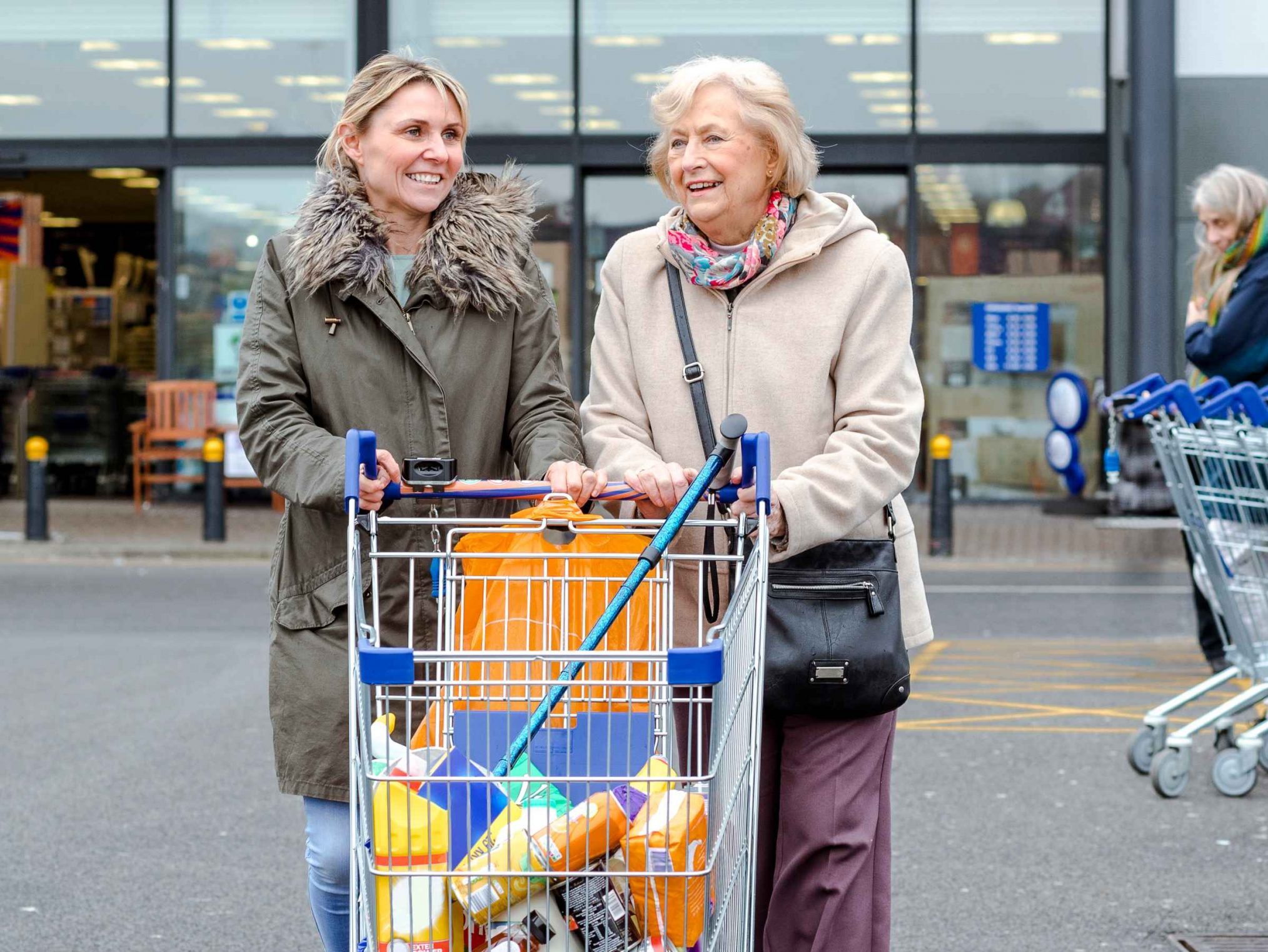 Aged person and support worker pushing shopping cart in carpark